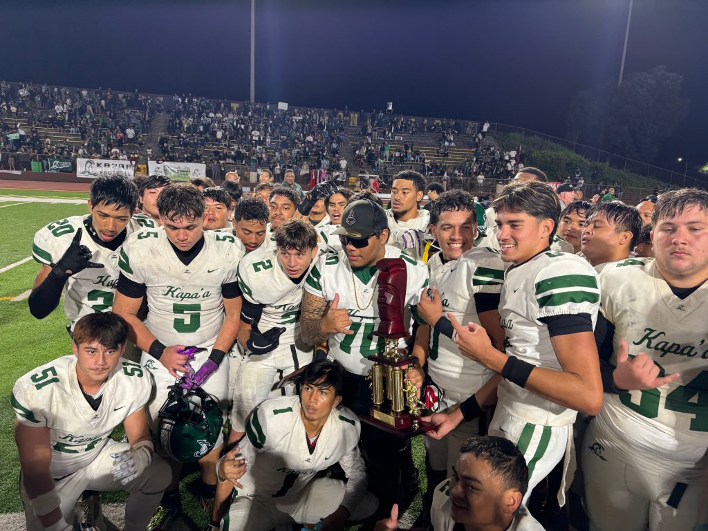 The Kapa'a High School football team poses with the First Hawaiian Bank/HHSAA Division I state championship trophy after the Warriors' 10-7 overtime win over Konawaena on Saturday. It is the first D-I title ever won by a Kauaʻi team on Nov. 30, 2024. (Rob Collias/Hawaiʻi Journalism Initiative)