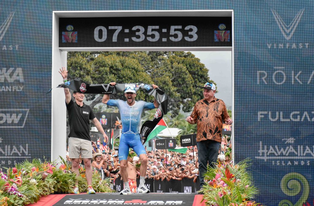 Patrick Lange of Germany celebrates after setting a Kona course record 7 hours, 35 minutes, 53 seconds on Saturday to win his third Ironman World Championship. Hawai'i Island mayor Mitch Roth (right) and Ironman CEO Scott DeRue hold the tape. (Cammy Clark/Big Island Now)